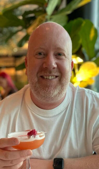 Dave Waller A photo of Dave looking happy, enjoying a meal and a fruit-based cocktail